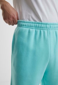 Light blue sweatpants with an elastic waistband, side pockets, and a soft texture, showing the waist area and hand grasping the waistband.