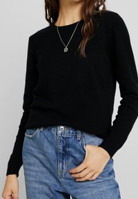 Schwarzer Pullover aus weichem Strickstoff, mit klassischem Rundhalsausschnitt und gerippten Bündchen, kombiniert mit hellblauen Jeans.