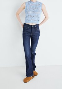 Ljusblå stickad topp med scallopkant och hexagonmönster, kombinerad med mörkblå rak benbyxor och bruna slip-on skor.