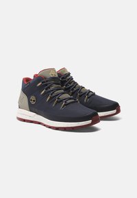 Granatowe trampki za kostkę z siateczkowym wierzchem, czerwonymi i złotymi akcentami, okrągłymi sznurówkami oraz nakrapianą białą podeszwą. Logo Timberland z boku.
