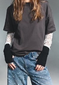 T-shirt scurt negru cu mâneci din dantelă albă; blugi denim albaștri rupți; mănuși negre fără degete; accente de inele argintii.