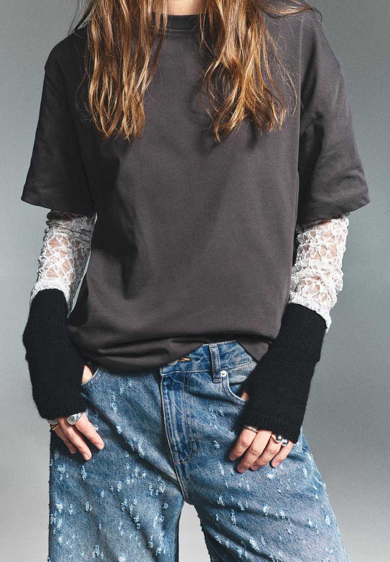 T-shirt scurt negru cu mâneci din dantelă albă; blugi denim albaștri rupți; mănuși negre fără degete; accente de inele argintii.