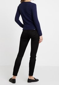 Maglione lavorato a maglia blu navy dal design aderente, abbinato a jeans neri slim-fit e mocassini neri. Tessuto liscio; silhouette sagomata.