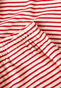 Tessuto di abbigliamento con righe orizzontali rosse e bianche e piccoli fori ad occhio, con una vita elastica.