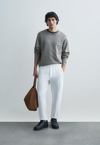 Sweatshirt cinzenta com detalhe de bolso, combinada com calças brancas afuniladas e ténis pretos. Uma bolsa tote castanha pendurada no pulso.