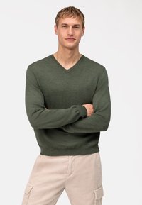 Groene V-hals trui van een textuur gebreide stof met geribde manchetten, gedragen over beige corduroy broeken, met een getailleerde pasvorm.