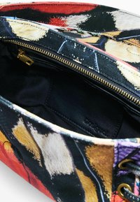 Geantă de pânză cu model floral în culori vibrante. Deschiderea cu fermoar dezvăluie un interior negru cu accente din piele și un patch cu logo.