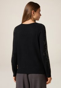 Maglione nero con maniche lunghe, scollo rotondo e decorazioni di perline sulle maniche; realizzato in un materiale morbido e testurizzato.