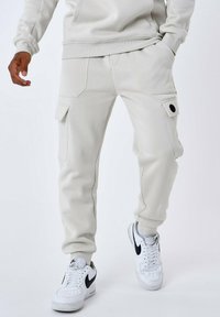 Pantalones jogger gris claro hechos de tela suave, con bolsillos laterales, un ajuste de pierna estrecha y puños acanalados, combinados con zapatillas blancas.