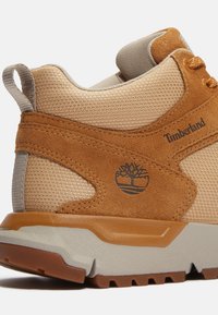 Sneaker color crema e marrone con tomaia in rete testurizzata, dettagli in camoscio, suola intermedia grigio chiaro e suola in gomma con logo a forma di albero.
