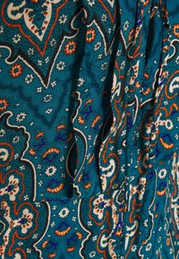Türkisfarbener Stoff mit einem Paisley-Muster, das orange und weiße Blumenakzente aufweist. Glatte Textur mit drapiertem Design und subtiler Schattierung.