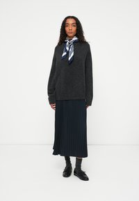 Ciemnoszary, oversize sweter o luźnym kroju, w zestawieniu z plisowaną granatową spódnicą. Uzupełniony paskiem w biało-granatowe paski. Na nogach czarne buty.