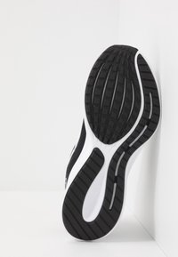 Schwarz-weiße Sportlersohlen mit strukturiertem Gummiprofil und seitlichen Rillen; entworfen für Griffigkeit und Flexibilität.