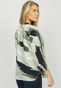 Langærmet bluse i let materiale med et abstrakt akvarelmønster i mint, sort og pink. Rundet kant og plisseringsdetaljer.