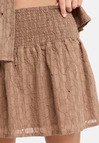 Bruine, textuur rok met een geplooide smock tailleband; heeft een cirkelpatroon en subtiele openingen in de stof. Lichtgewicht materiaal.