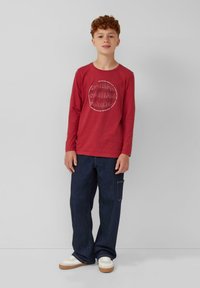 Rode longsleeve T-shirt met een grafische print met "SOUND" in een circulair ontwerp. Draag het met donkerblauwe baggy jeans en witte sneakers.