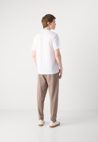 White short-sleeve t-shirt, relaxed fit, paired with beige trousers. Footwear: white, low-profile sneakers with light brown soles.