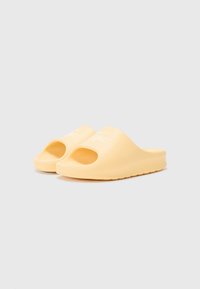 Sandales jaunes en matériau doux, avec bout ouvert, bords arrondis et semelle extérieure texturée. Comprend un détail de logo discret.