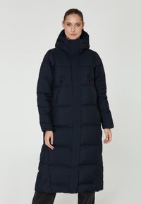 Abrigo largo acolchado en azul marino con un cuello alto, costuras verticales, capucha y bolsillos con cremallera. Confeccionado en una suave tela texturizada para proporcionar calor.
