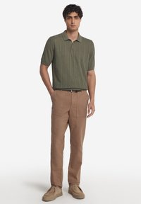 Olivgrönstickad polo med vertikala ränder, kombinerad med tan cargo-byxor med sidfickor och ljusbruna slip-on skor.