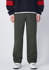 Grüne weite Hosen aus leichtem Stoff, kombiniert mit einem navyblauen und roten gestreiften Strickpullover. Weiße Sneaker runden das Outfit ab.