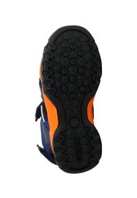 Suela de zapato de goma negra con patrones de huella circulares, presenta un acento naranja en los laterales y una superficie texturizada para un mejor agarre.
