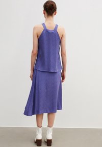 Lila ärmlös topp och matchande kjol med en vågig textur. Modellen bär vita ankelboots med klack.