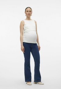Graviditetströja i vitt, med en kroppsnära design. Parat med blå, utställda jeans och beigefärgade ballerinas. Enkel och avslappnad look.