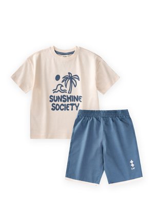 Beiges T-Shirt mit kurzen Ärmeln, Palmen- und Wellen-Grafik sowie "Sunshine Society" Text, kombiniert mit blauen Shorts mit elastischem Bund.