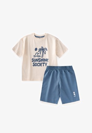 Beżowy t-shirt z krótkim rękawem z grafiką palmy i fali oraz tekstem "Sunshine Society", w połączeniu z niebieskimi szortami z elastycznym pasem.