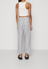 Ljust grå, randiga byxor med avslappnad passform och elastisk midja. Kombinationen med en vit, ärmlös crop top och svarta sandaler.