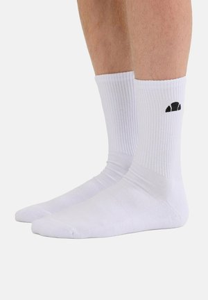 Paar weiße Sportsocken am Fuß getragen, mit Rippenstruktur, schwarzes Logo an der Außenseite des rechten Sockens, vor hellem einfarbigem Hintergrund.