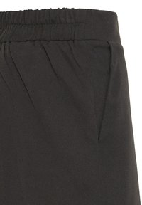 Acercamiento al tejido de pantalones negros con cintura elástica y detalle de la costura del bolsillo lateral.