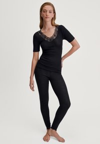Zwarte top met kant V-hals en korte mouwen, gecombineerd met bijpassende zwarte leggings. De stof lijkt zacht en aansluitend, met subtiele textuurdetails.