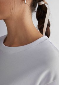 Vit crew-neck sweatshirt med en texturerad yta, med en ribbad krage och mjukt tyg. Hår som är uppsatt med ett ljust band syns.