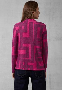 Fuchsia trui met een geometrisch patroon in donkerpaars. Lange mouwen en een hoge hals, met een rechte zoom en zijsplitten.