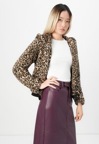 Faux fur bomber jacket in leopard print, featuring a black ribbed hem and cuffs. Paired with a fitted white top and a burgundy leather skirt.