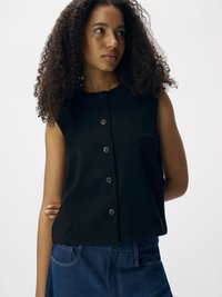 Blusa sin mangas negra con escote redondo, cierre frontal con botones y una textura suave, combinada con una falda de mezclilla azul.