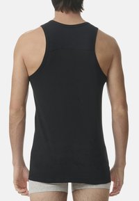 Svart bomullstopp med låg rygg, breda ärmhål och en slät textur. Sömmen är något rundad, med synliga stygn detaljer.