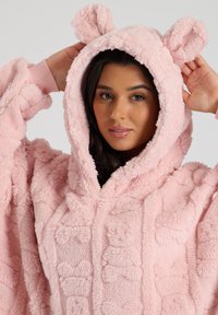 Felpa oversized rosa in peluche con un motivo di pelliccia testurizzata, orecchie da orso sul cappuccio e polsini a coste. Il materiale morbido offre calore e comfort.