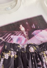 Sweat crème avec motif floral rose, associé à une jupe foncée à taille élastique avec des motifs floraux violet clair et verts.