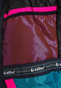 Innere Netz-Tasche mit pinkem, rotem und schwarzem Muster, eingefasst von pinkem Stoff und schwarzem Rand auf einem türkisfarbenen und schwarzen Kleidungsstück.