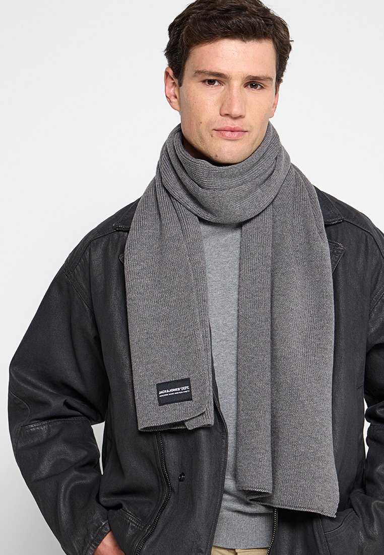 Grauer gestrickter Schal mit Rippstruktur, um den Hals gewickelt. Verfügt an einem Ende über ein schwarzes Etikett, das die Marke kennzeichnet.