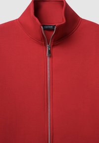 Giacca rossa con zip, dotata di un alto colletto, realizzata in un tessuto morbido. Presenta una zip argentata e una piccola etichetta del marchio all'interno del colletto.