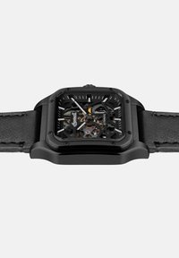 Skelett-Automatik-Uhr mit schwarzem quadratischem Gehäuse, kontrastierenden weißen Stundenmarkierungen und einem strukturierten schwarzen Lederarmband.