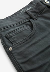 Jeans negri din denim cu un buzunar frontal, buton metalic și detalii de cusătură. Materialul are un aspect neted și texturat.