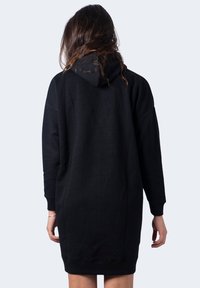 Abito felpa nero con una texture morbida, maniche lunghe e cappuccio. Presenta una vestibilità ampia e arriva a metà coscia. Senza loghi visibili.