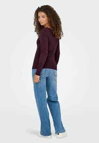 Maglia a maniche lunghe, aderente di colore marrone porpora abbinata a jeans a gamba larga celesti. I jeans hanno un finish sbiadito e un design classico a cinque tasche.
