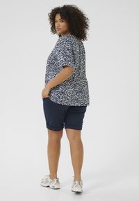 Top corto a maniche corte blu navy e bianco a fantasia abbinato a pantaloni corti blu scuro. Modella con scarpe da ginnastica grigio chiaro e capelli acconciati in ricci.