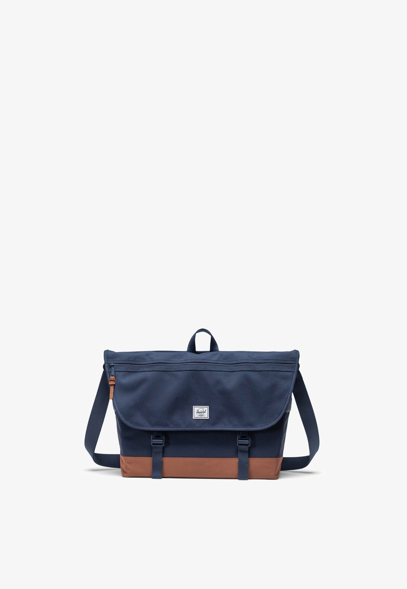 Borsa a messenger navy con pannello inferiore marrone. Realizzata in tessuto con chiusura a pattina, presenta una toppa con logo, una tasca frontale con cerniera e una tracolla regolabile.